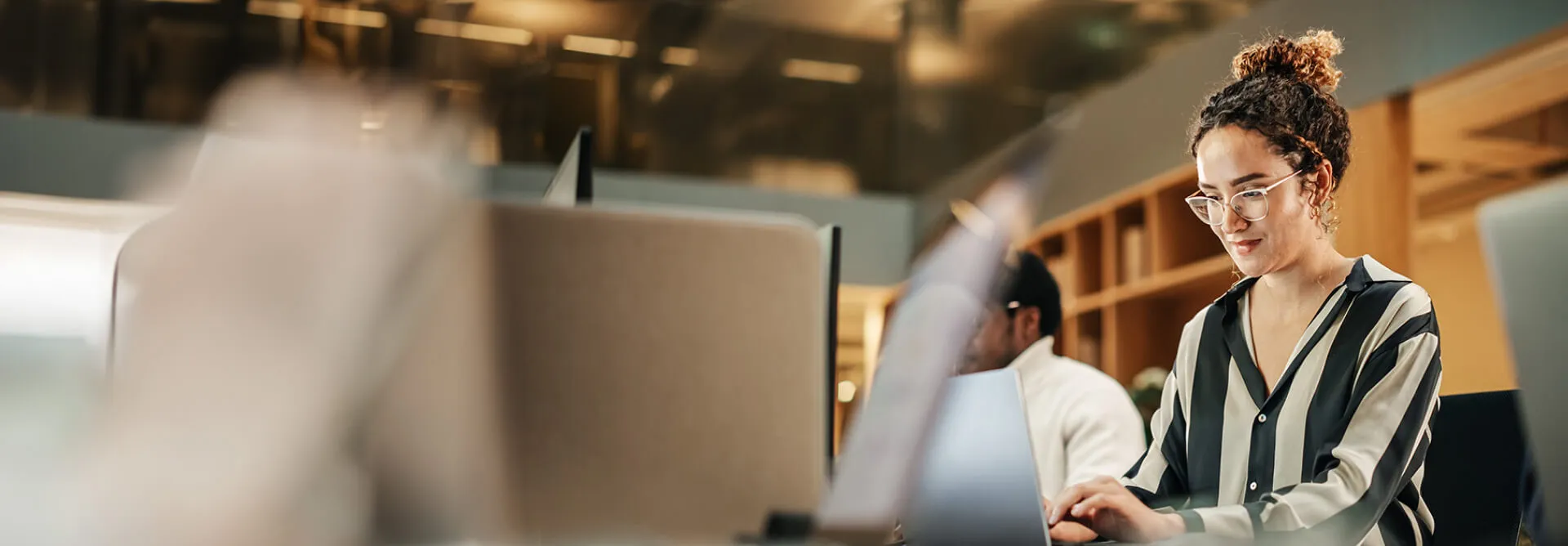 A woman wearing glasses looks at her laptop in a coworking space