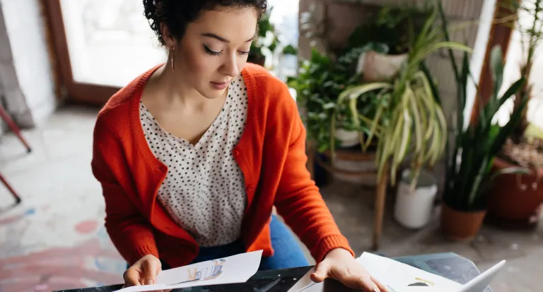 A woman in an orange cardigan looks through sketches on paper