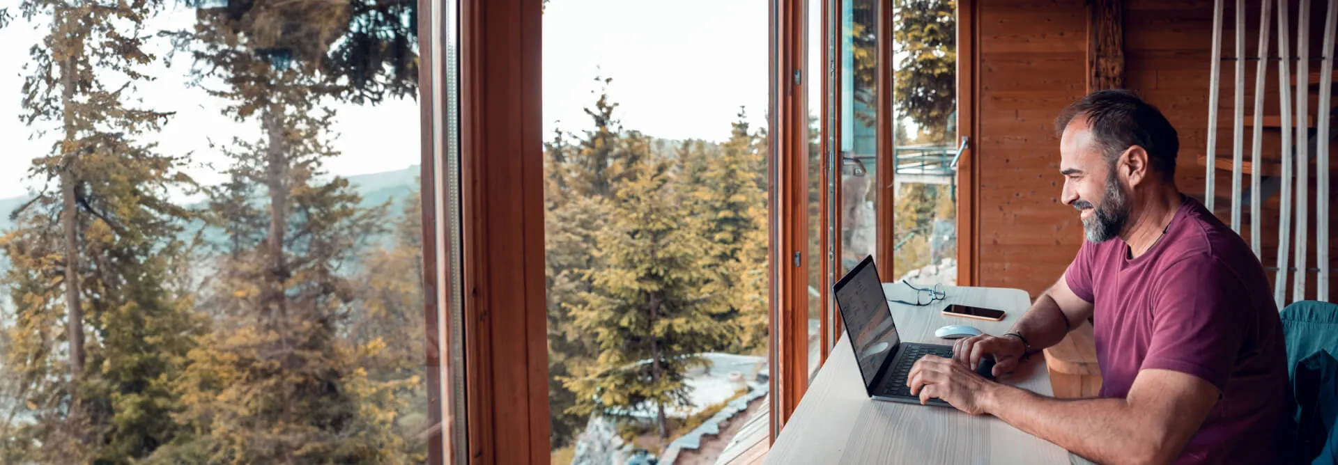 A man works as he's sitting in a cabin style room surrounded by woodland