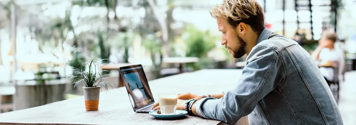 Man sits in an large open café with a latte and his laptop