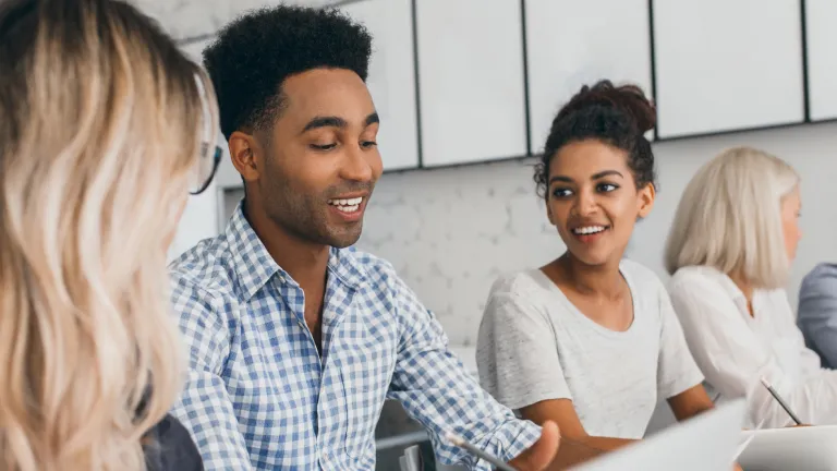A smartly dressed man sat at a desk talking to two women.