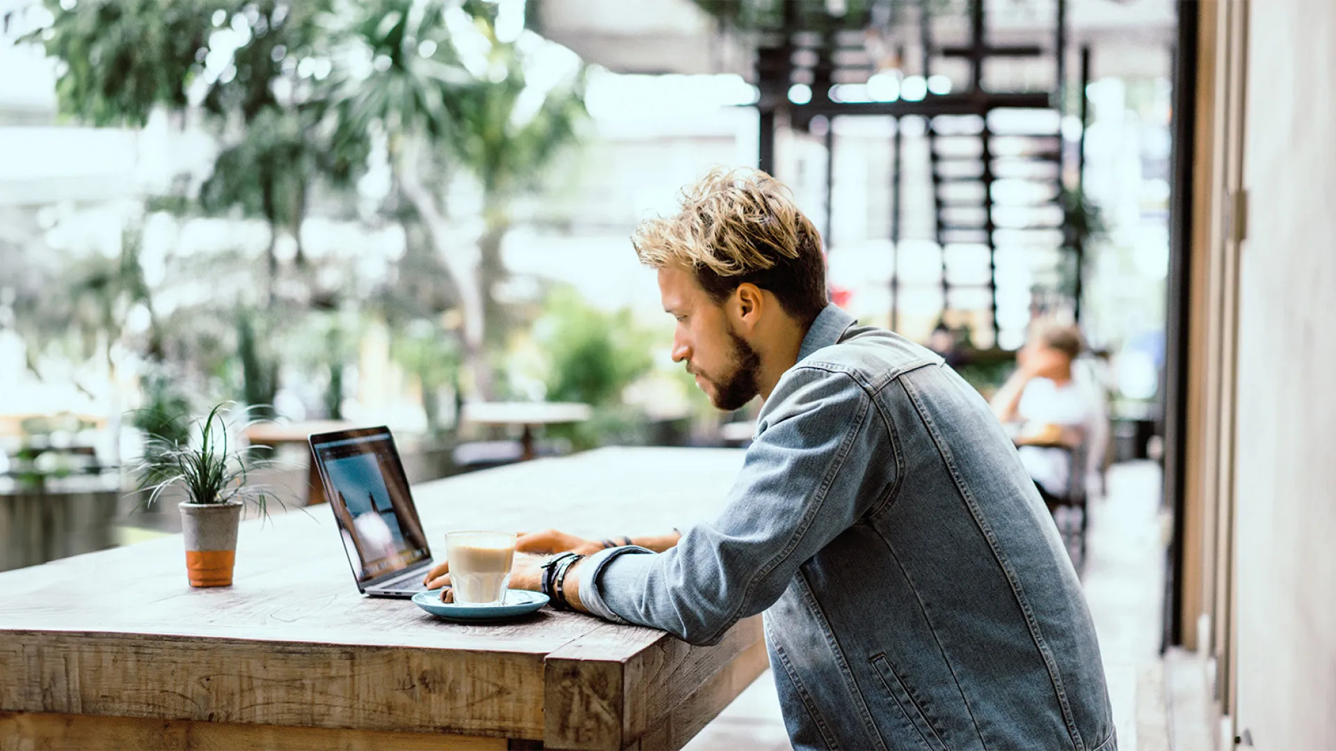 Man sits in an large open café with a latte and his laptop