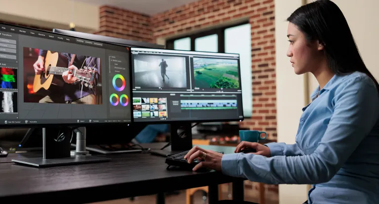 Woman works on editing software across two computer monitors