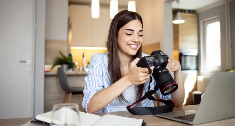 Woman sitting in her kitchen looks through photos on her camera 