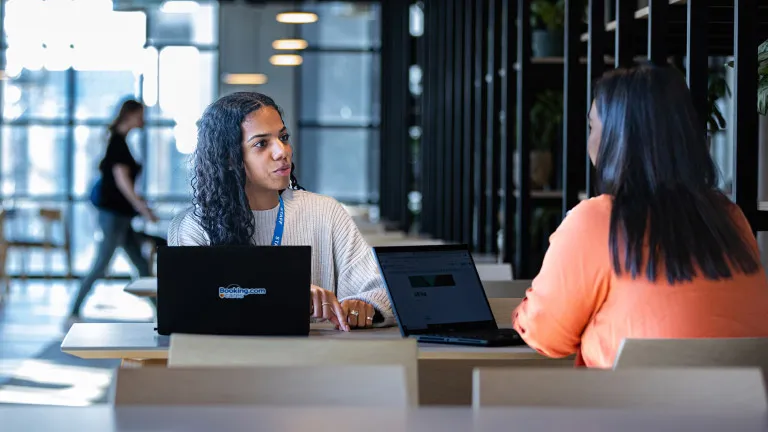 Two female employees sit at a table with their laptops