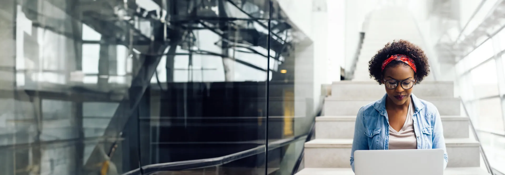 A woman smiles at her laptop as she sits on stairs of an office